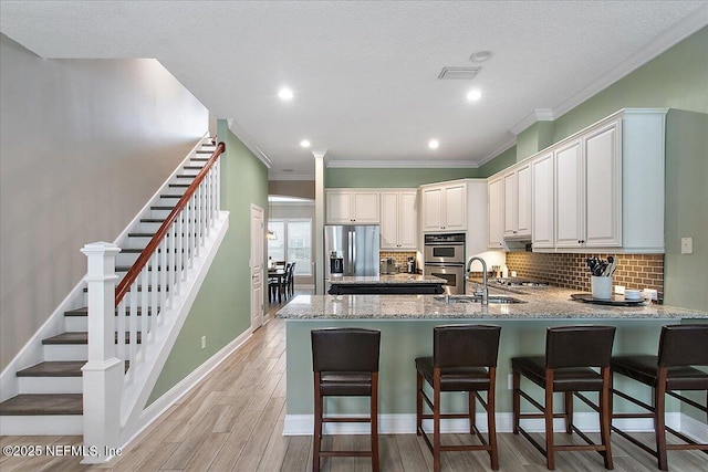 kitchen featuring white cabinets, light wood-style flooring, appliances with stainless steel finishes, a kitchen bar, and a sink