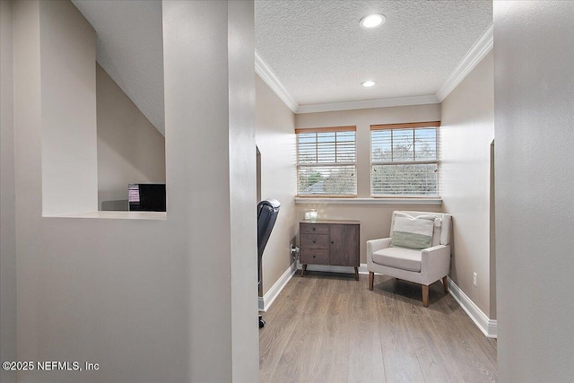 living area with baseboards, crown molding, light wood-style flooring, and a textured ceiling