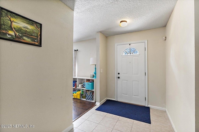 foyer featuring light tile patterned floors, a textured ceiling, and baseboards