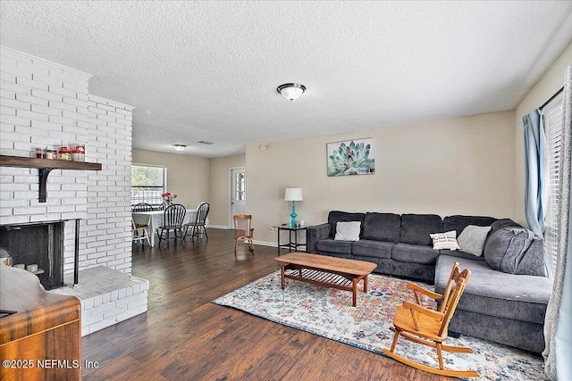 living room featuring a brick fireplace, a textured ceiling, baseboards, and wood finished floors