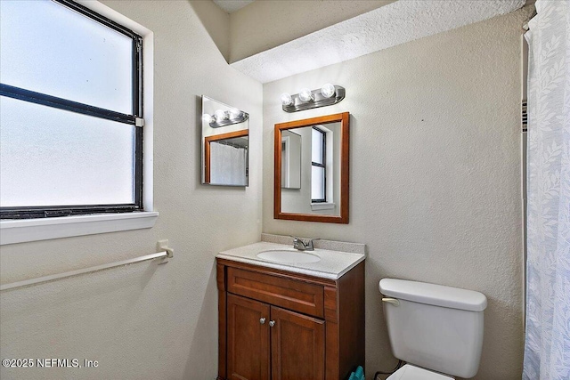 bathroom featuring a textured wall, vanity, and toilet