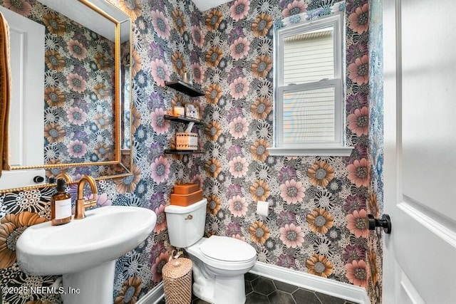 half bathroom featuring baseboards, a sink, toilet, and wallpapered walls