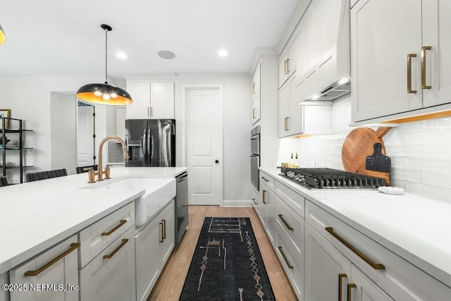 kitchen featuring stainless steel appliances, a sink, hanging light fixtures, light countertops, and custom exhaust hood