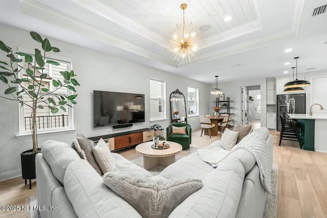 living area with light wood-style floors, a tray ceiling, plenty of natural light, and an inviting chandelier