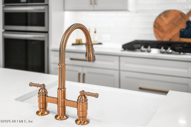details featuring double oven, cooktop, a sink, white cabinetry, and light countertops