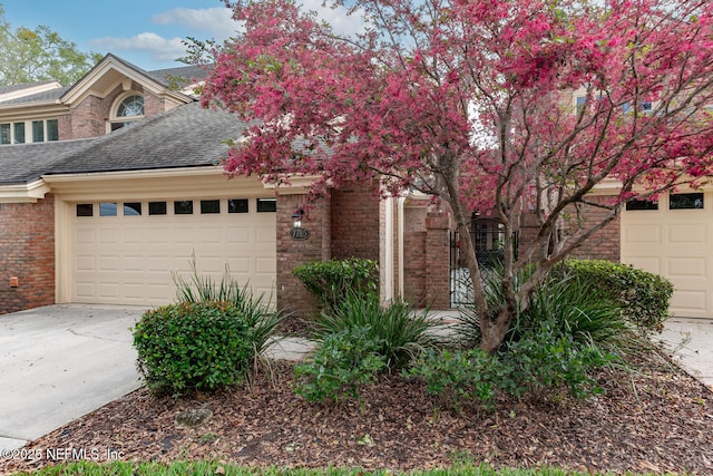 view of front of home with an attached garage, driveway, a shingled roof, and brick siding