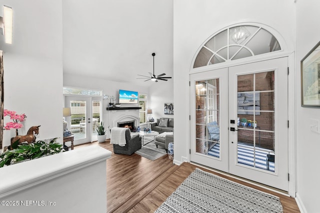 foyer entrance with french doors, a lit fireplace, a high ceiling, and wood finished floors