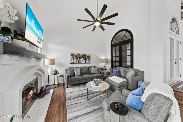 living area with french doors, a fireplace, a high ceiling, a ceiling fan, and wood finished floors