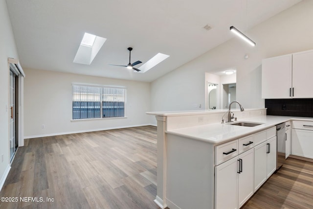 kitchen featuring vaulted ceiling with skylight, sink, white cabinets, stainless steel dishwasher, and light wood-type flooring