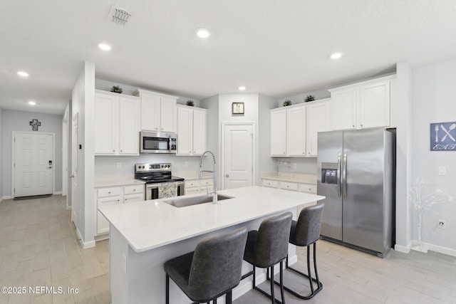 kitchen featuring a center island with sink, light countertops, appliances with stainless steel finishes, white cabinetry, and a sink