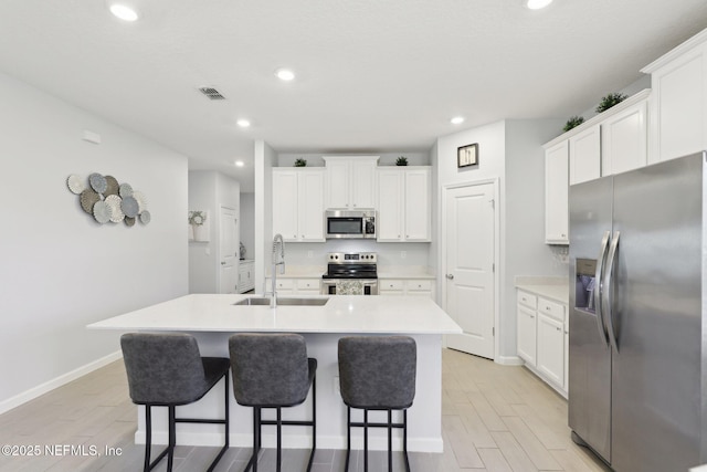 kitchen featuring a center island with sink, visible vents, a sink, stainless steel appliances, and white cabinetry