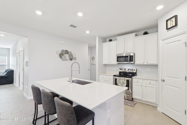 kitchen with a sink, stainless steel appliances, an island with sink, and light countertops