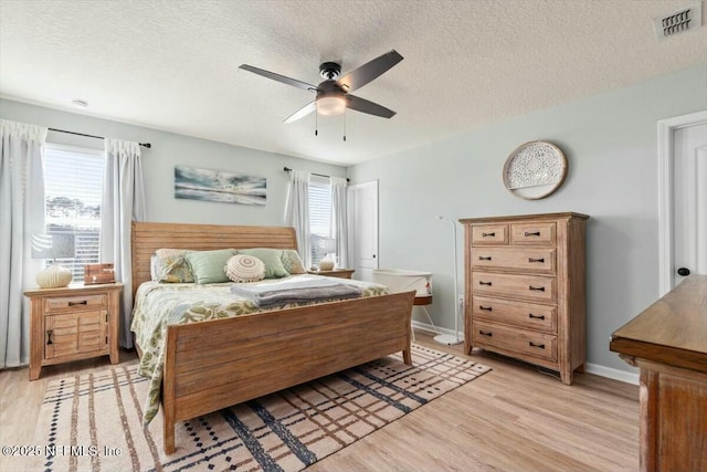 bedroom with light wood-type flooring, multiple windows, visible vents, and a textured ceiling