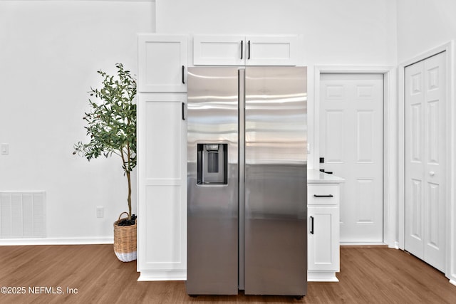 kitchen with white cabinets, stainless steel fridge, visible vents, and wood finished floors