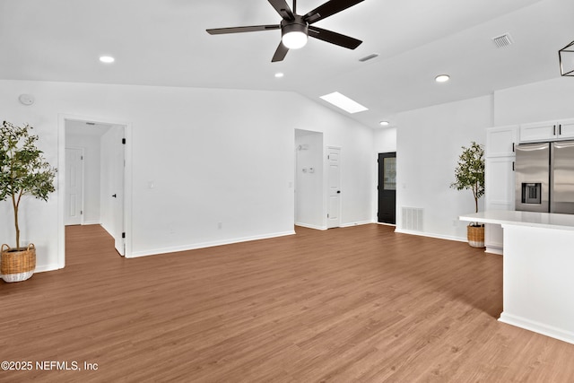 unfurnished living room featuring vaulted ceiling with skylight, light wood finished floors, and visible vents