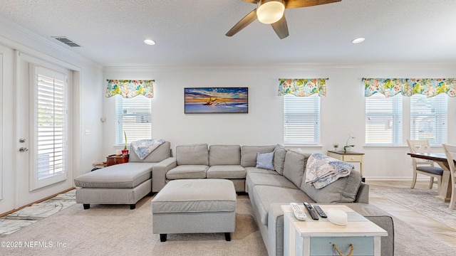 living room featuring plenty of natural light, visible vents, a textured ceiling, and ornamental molding