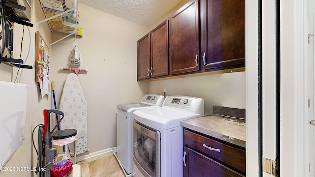 clothes washing area featuring baseboards, cabinet space, a textured ceiling, and washing machine and clothes dryer