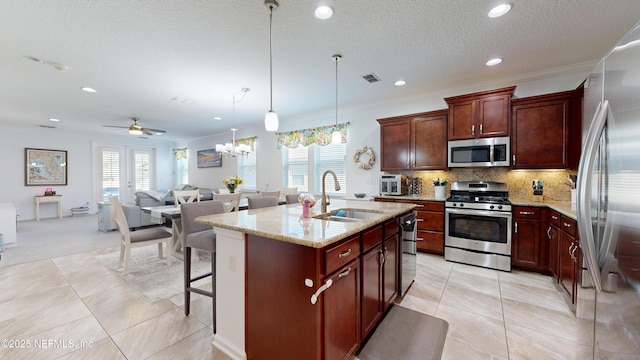 kitchen featuring decorative backsplash, appliances with stainless steel finishes, a sink, light stone countertops, and a kitchen bar