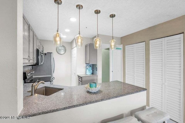 kitchen featuring appliances with stainless steel finishes, decorative light fixtures, sink, a kitchen bar, and kitchen peninsula