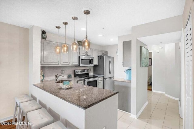 kitchen with a kitchen bar, hanging light fixtures, dark stone counters, kitchen peninsula, and stainless steel appliances