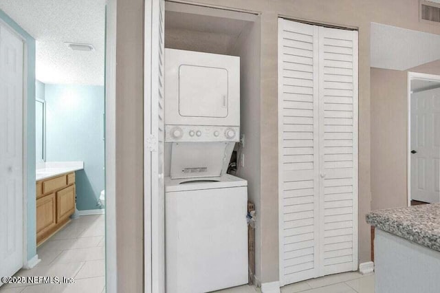 washroom featuring light tile patterned flooring, stacked washer / dryer, and a textured ceiling