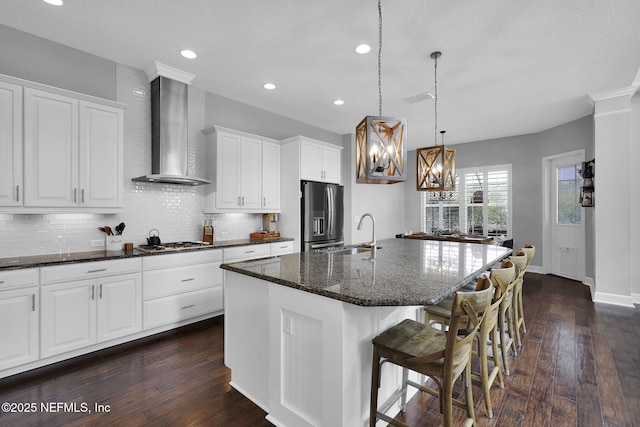 kitchen featuring a kitchen island with sink, stainless steel appliances, sink, white cabinets, and wall chimney range hood