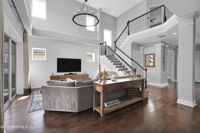 living room with a notable chandelier, dark wood-type flooring, decorative columns, and a towering ceiling