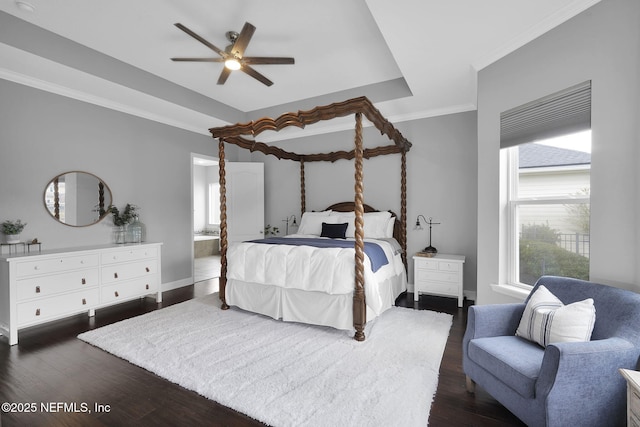 bedroom with a raised ceiling, ensuite bathroom, crown molding, and dark wood-type flooring