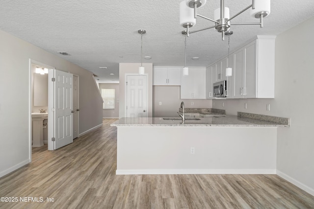 kitchen featuring sink, light stone counters, white cabinetry, light hardwood / wood-style floors, and kitchen peninsula