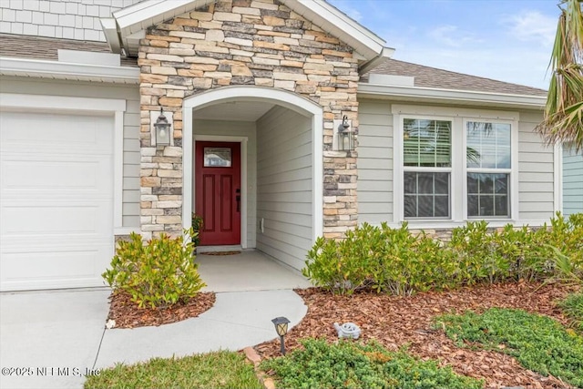 entrance to property with a garage, stone siding, and roof with shingles