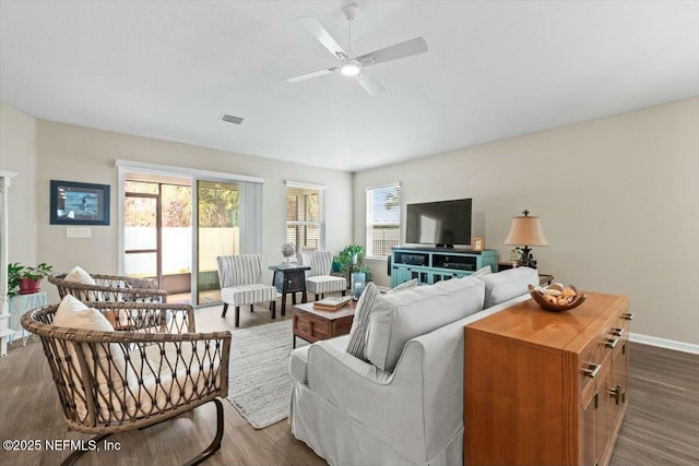 living area featuring a healthy amount of sunlight, ceiling fan, visible vents, and dark wood-type flooring