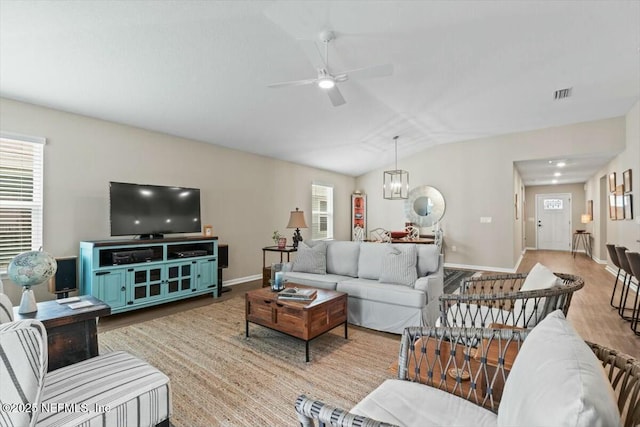 living room with visible vents, light wood-style floors, vaulted ceiling, baseboards, and ceiling fan with notable chandelier