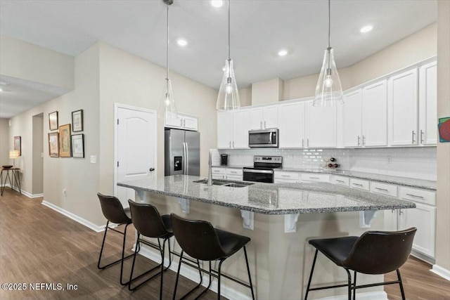 kitchen featuring an island with sink, appliances with stainless steel finishes, a kitchen bar, white cabinetry, and a sink