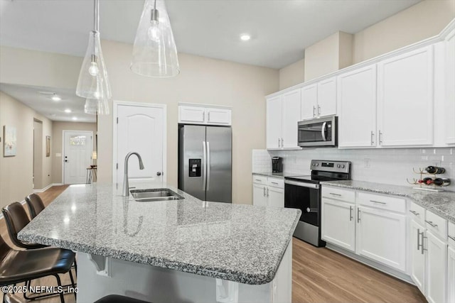 kitchen with a center island with sink, a breakfast bar, stainless steel appliances, white cabinetry, and a sink