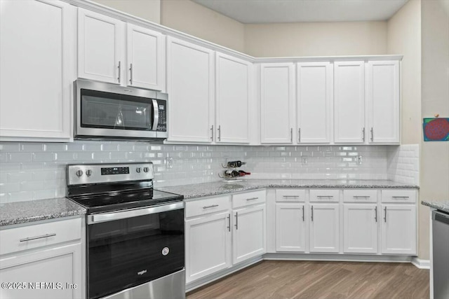 kitchen featuring stainless steel appliances, decorative backsplash, white cabinetry, light stone countertops, and light wood-type flooring