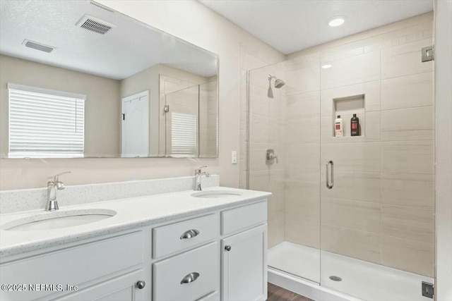 bathroom with double vanity, a sink, visible vents, and a shower stall