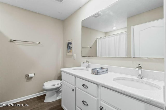 full bathroom with double vanity, toilet, a sink, and wood finished floors