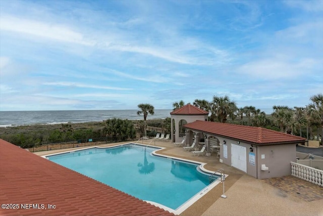 pool with a patio area, a water view, and fence