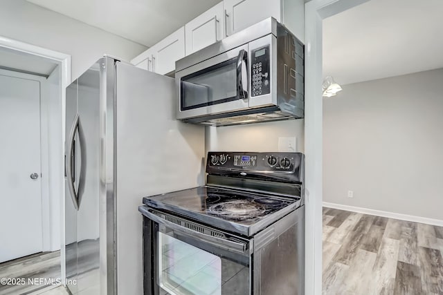 kitchen featuring hanging light fixtures, black range with electric stovetop, white cabinets, and light wood-type flooring