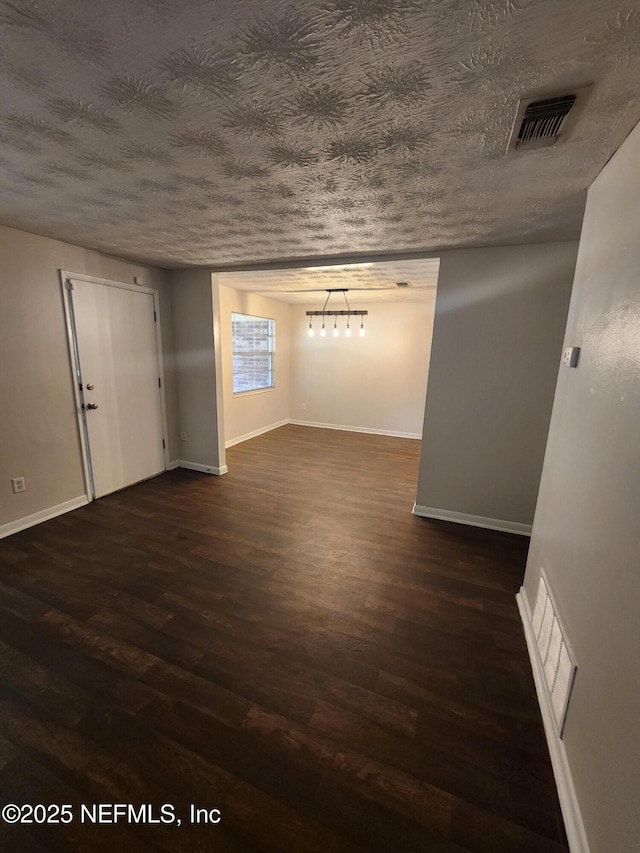 interior space with a textured ceiling, dark wood-type flooring, and visible vents