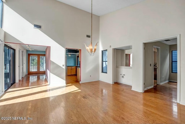 interior space featuring light hardwood / wood-style floors, french doors, a chandelier, and a high ceiling