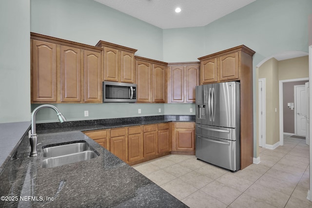 kitchen with arched walkways, light tile patterned floors, appliances with stainless steel finishes, a sink, and dark stone counters