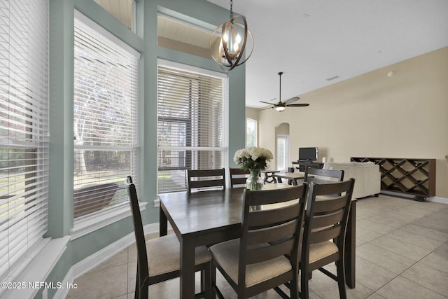 dining area with ceiling fan with notable chandelier, arched walkways, baseboards, and light tile patterned floors