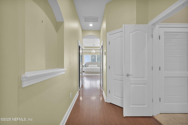 hallway featuring arched walkways, visible vents, baseboards, and wood finished floors