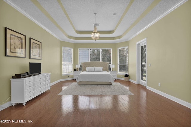 bedroom featuring baseboards, visible vents, hardwood / wood-style floors, a tray ceiling, and a chandelier