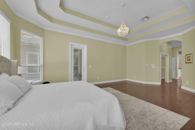 bedroom featuring arched walkways, wood finished floors, visible vents, a tray ceiling, and an inviting chandelier