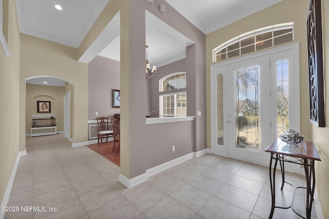 foyer featuring light tile patterned floors, ornamental molding, arched walkways, and baseboards