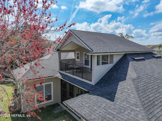 rear view of house featuring roof with shingles, a balcony, and stucco siding