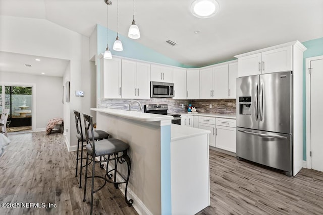 kitchen featuring vaulted ceiling, visible vents, stainless steel appliances, and a breakfast bar area