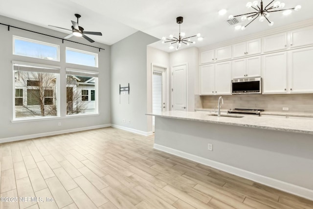 kitchen featuring pendant lighting, stainless steel microwave, white cabinets, a sink, and light stone countertops